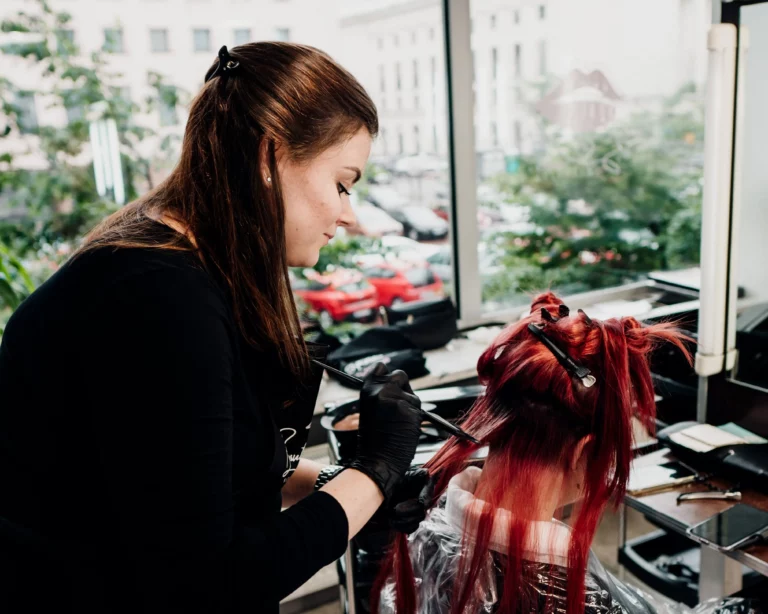 Młoda dziewczyna farbuje włosy na czerwono na kursie fryzjrstwa
