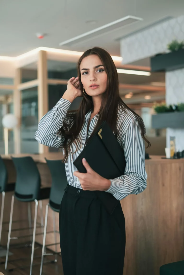 Kobieta z długimi włosami prezentuje elegancki makijaż biznesowy w nowoczesnym wnętrzu biura.