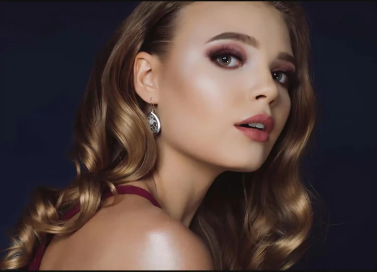 Zbliżenie na twarz kobiety w makijażu sylwestrowym z elegancką fryzurą i błyszczącą cerą oraz klasycznymi kolczykami.