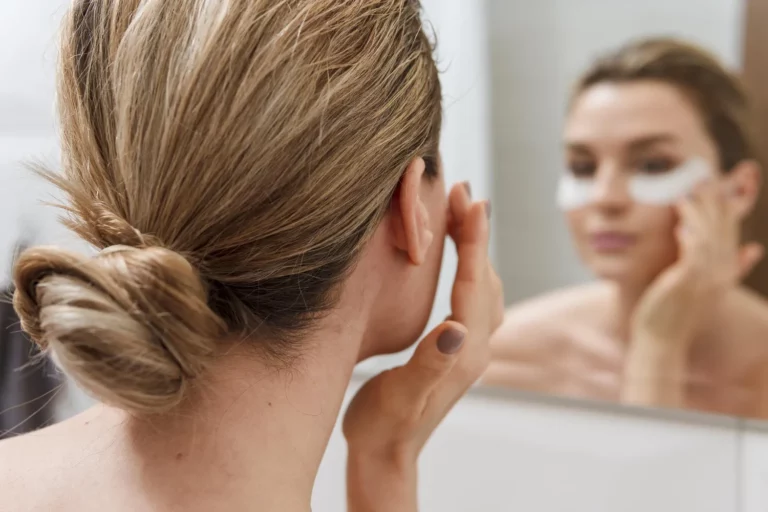Kobieta przed lustrem nakłada płatki pod oczy w trakcie pielęgnacji, element przygotowania cery nauczany w szkoła wizażu Warszawa oraz na kurs makijażu Warszawa