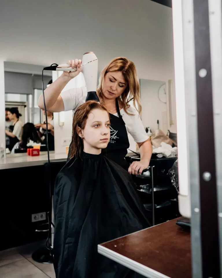 Instruktorka suszy włosy modelce podczas zajęć praktycznych, jakie oferuje szkoła fryzjerska Warszawa w ramach kurs fryzjerski Warszawa.